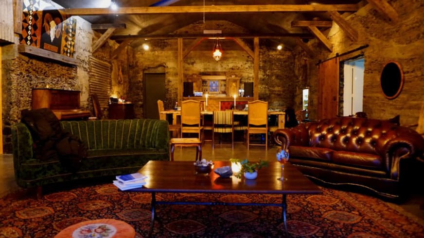 Rustikaler Gastraum der Holy Ram Lodge mit Natursteinwänden, Chesterfield-Sofas und Kamin für gemütliche Abende.