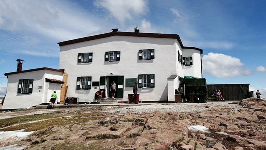 Das Schutzhaus Rittner Horn steht auf felsigem Bergplateau mit Besuchern auf der Terrasse.