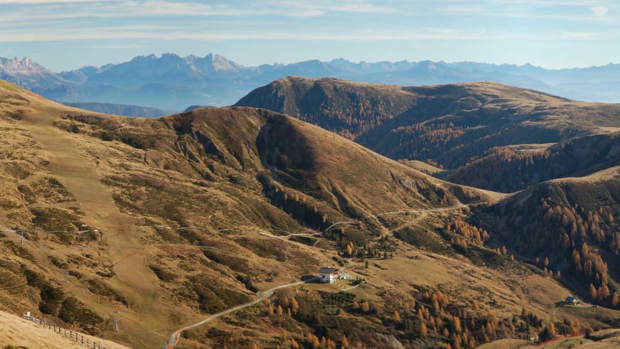 Panoramaaufnahme zeigt die Meraner Hütte inmitten herbstlicher Berglandschaft mit warmen Farbtönen und sanften Hügeln.