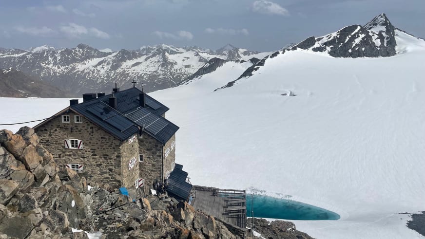 Das Brandenburger Haus steht auf einem schneebedeckten Gletscher mit türkisfarbenem Wassertank und Bergpanorama.