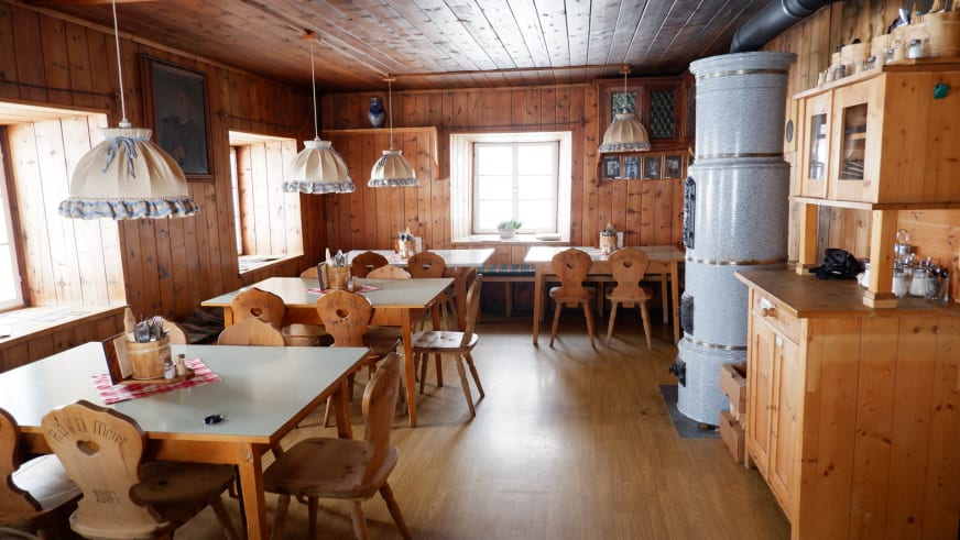 Gaststube im Brandenburger Haus zeigt vollständige Holzverkleidung mit Almstühlen und Kachelofen.