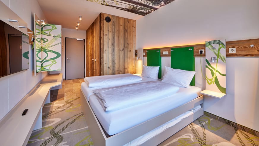 Modernes Doppelzimmer im Explorer Hotel Stubaital mit grünem Kopfteil und Holzverkleidung.
