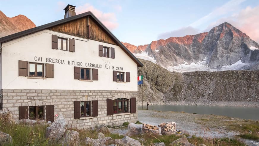 Das Rifugio Giuseppe Garibaldi steht auf 2.550 m Höhe vor einer verschneiten Felswand in der Adamello-Gruppe.