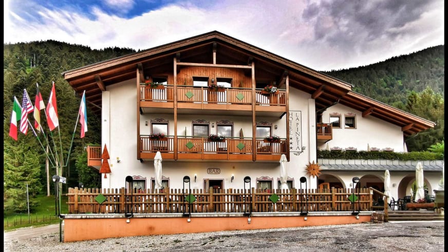 Das Hotel Pizzeria La Pineta zeigt sich als dreistöckiges Alpenhotel mit weißer Fassade und Holzbalkonen in Tiroler Baus