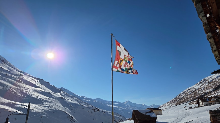 Blick von der Pension Edelweiss Juf über das verschneite Averstal mit Schweizer Flagge und Bergpanorama der Oberhalbstei