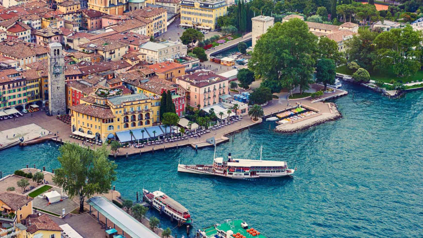 Zwei weiße Ausflugsschiffe fahren vor der Altstadt von Riva mit den Garda Hotels Riva **** am Seeufer.