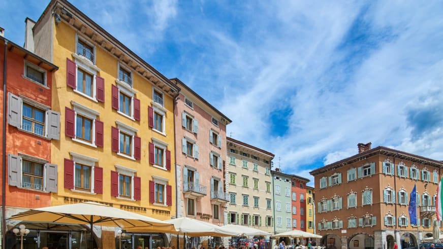 Historischer Stadtplatz in Riva mit bunten Gebäuden der Garda Hotels Riva **** und Straßencafés mit Sonnenschirmen.