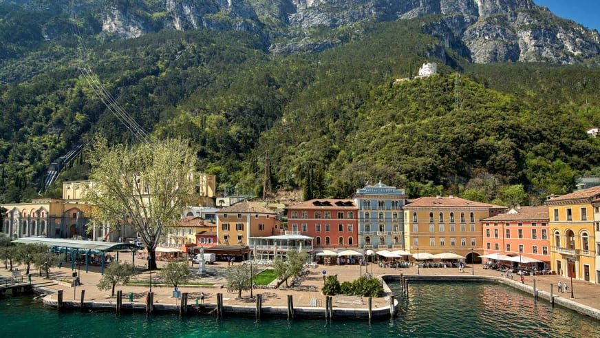 Hafenpromenade in Riva mit pastellfarbenen Fassaden der Garda Hotels Riva **** und Holzstegen am Gardasee.