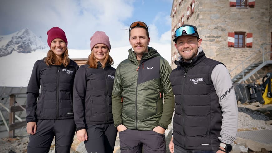 Das Hüttenteam der Neuen Prager Hütte steht vor dem Steingebäude in winterlicher Berglandschaft der Hohen Tauern.
