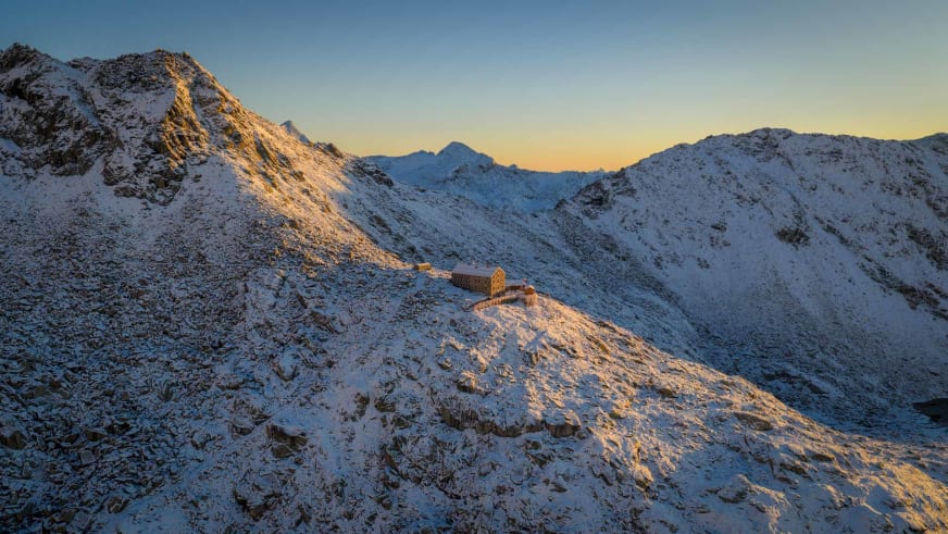 Panoramaaufnahme der Neuen Prager Hütte während der goldenen Stunde vor verschneiter Bergkulisse der Hohen Tauern.