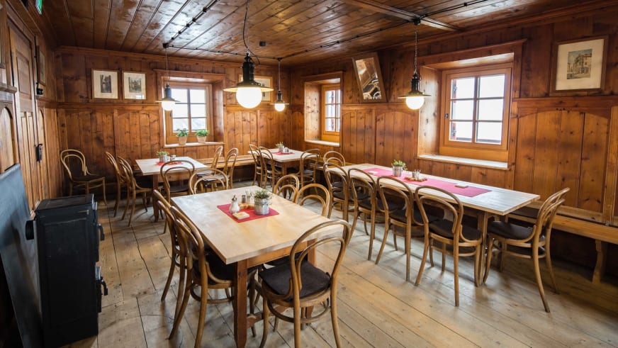 Der gemütliche Gastraum der Neuen Prager Hütte mit Holzvertäfelung, Thonet-Stühlen und traditioneller Alpeneinrichtung.