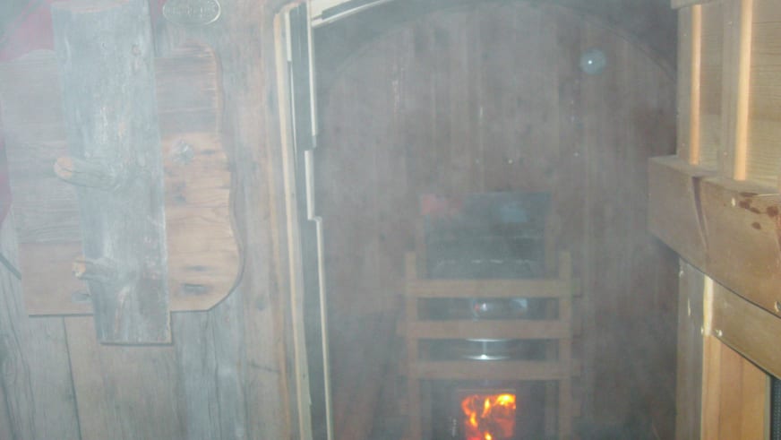 Innenraum der Sauna im Rifugio Lavarella mit gemauertem Holzofen, Dampf und traditioneller Holzausstattung.