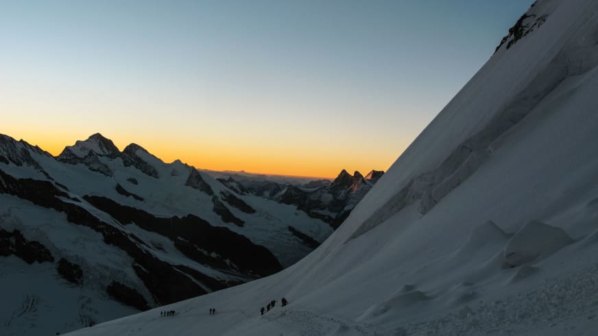 Bergsteiger-Seilschaft steigt bei Sonnenaufgang durch Gletscherhänge nahe der Mönchsjochhütte in den Berner Alpen auf.