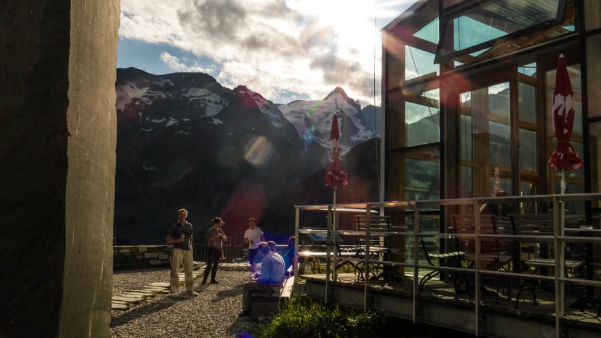 Terrasse von Das Glocknerhaus mit Personen und Ausblick auf die schneebedeckten Berggipfel der Hohen Tauern bei warmer Lichtstimmung.