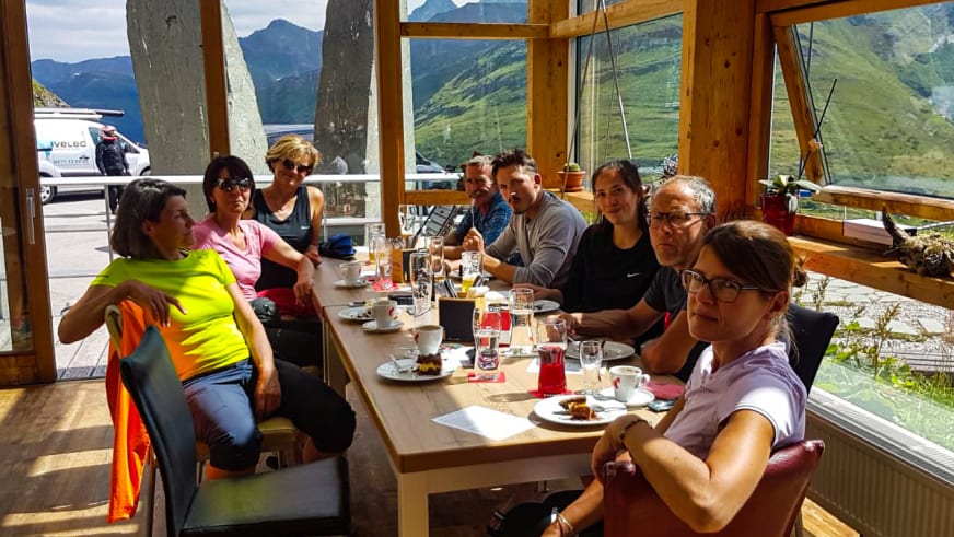 Im Gastraum des Glocknerhaus sitzen Wanderer am Holztisch vor großen Fenstern mit Blick auf die Berglandschaft.