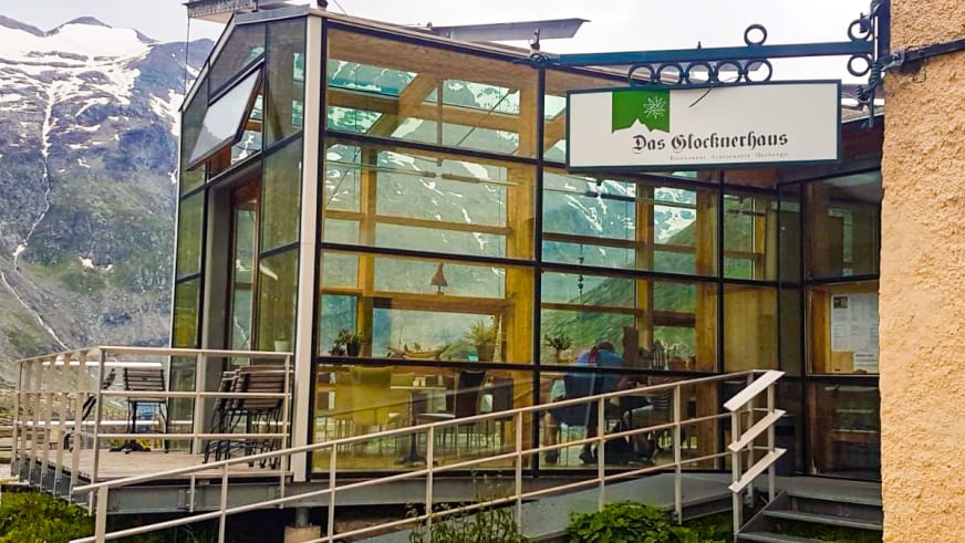 Das moderne Glocknerhaus zeigt seine Glasfassade mit Holzrahmen und Terrasse vor verschneiter Bergkulisse.