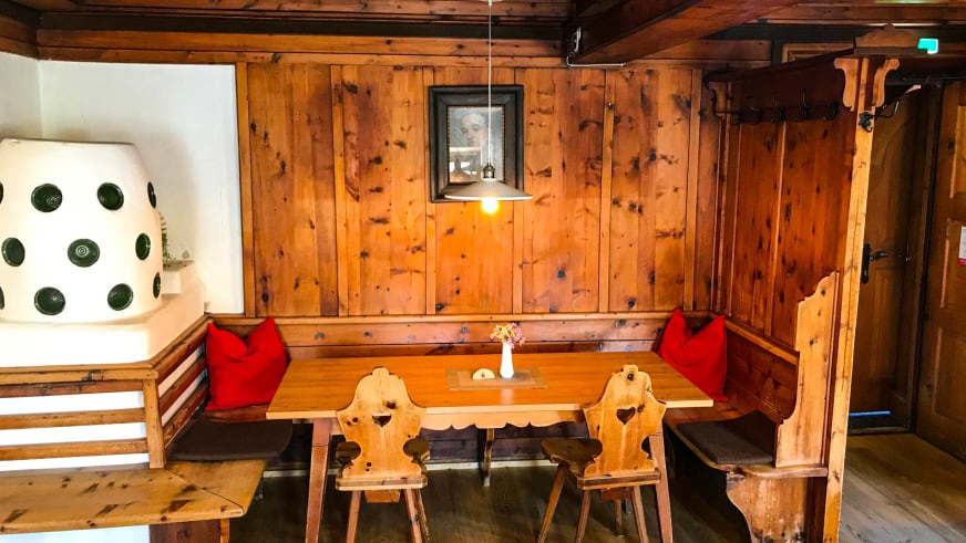 Gemütlicher Gastraum im Hochjoch Hospiz mit Eckbank, Kachelofen und traditioneller Holzvertäfelung.