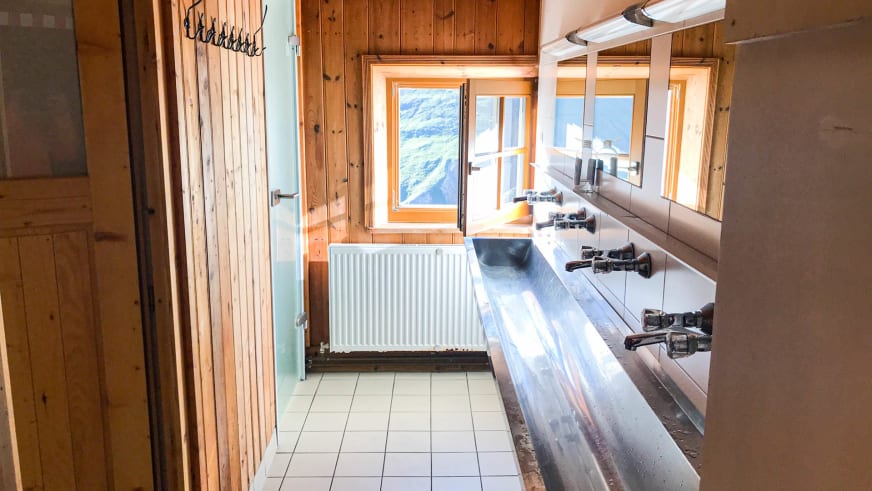 Funktionaler Skiraum im Hochjoch Hospiz mit türkisfarbenen Spinden und Skistiefelablagen am Fenster.