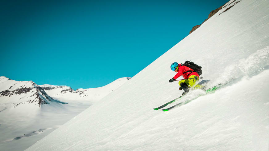 Ein Skifahrer fährt steilen Pulverhang bei Brimnes Hotel and Cabins in Islands Bergwelt ab.