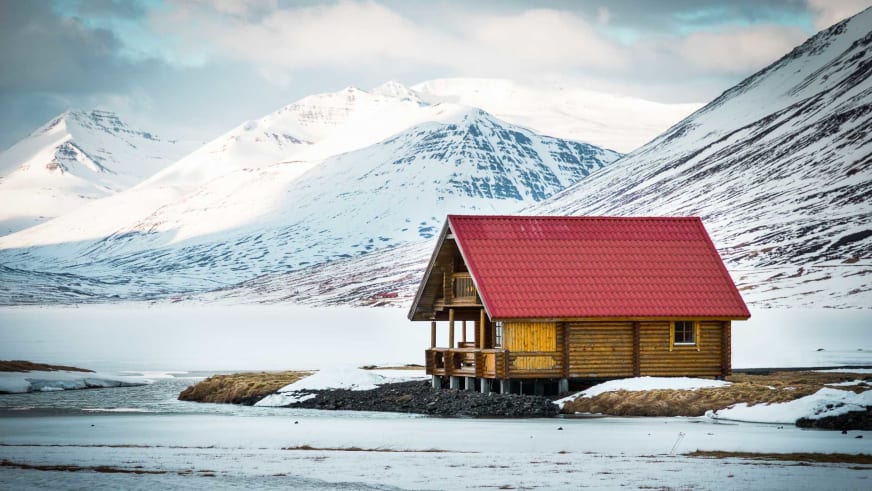 Einzelne Holzhütte des Brimnes Hotel and Cabins steht am Fjordufer in Islands Winterlandschaft.