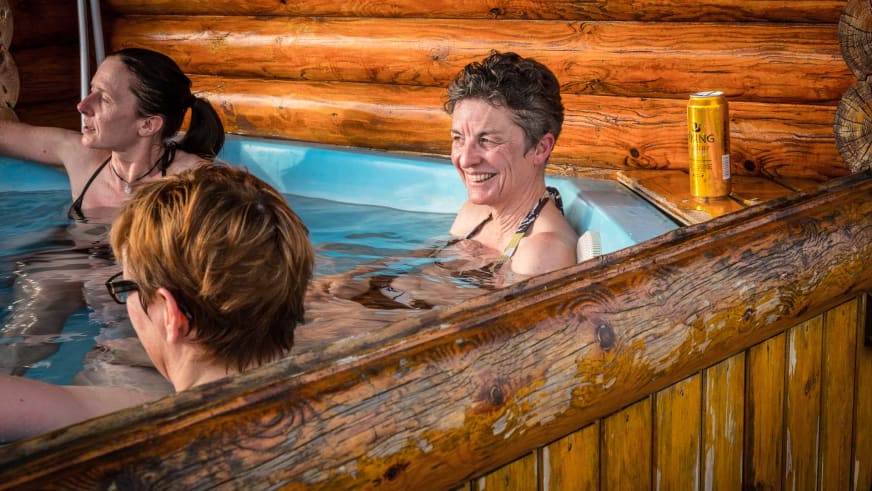 Drei Personen entspannen im Holz-Whirlpool des Brimnes Hotel and Cabins mit türkisblauem Wasser in Island.