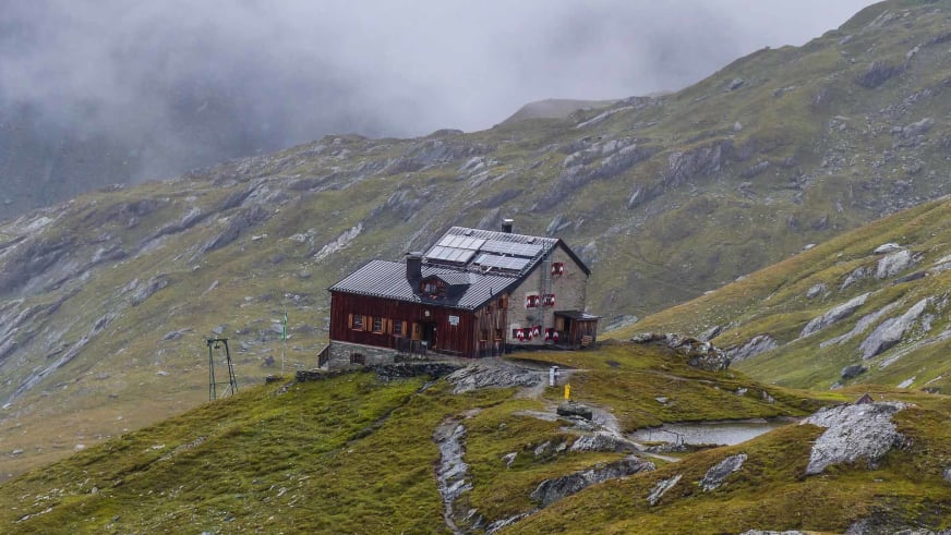 Panoramablick auf die Sudetendeutsche Hütte mit Wellblechdach und Solarpaneelen auf grasbewachsener Hochalm.