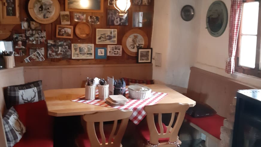 Traditioneller Gastraum der Stöfflhütte mit Holztisch, Kachelofen und alpiner Wanddekoration.