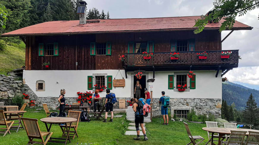 Wandergruppe mit Rucksäcken vor dem Chalet refuge de Nant Borrant, einem zweistöckigen Alpenchalet mit Holzbalkon und Außenterrasse.