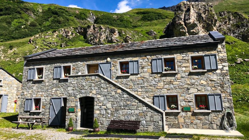 Das Refuge des Mottets mit traditioneller Steinarchitektur und blauen Fensterläden steht auf einer gepflasterten Fläche 