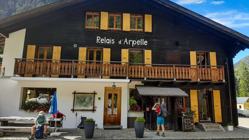 Das Relais d'Arpette zeigt sich als zweistöckige Berghütte mit dunkler Holzfassade und gelben Fensterläden am gepflaster