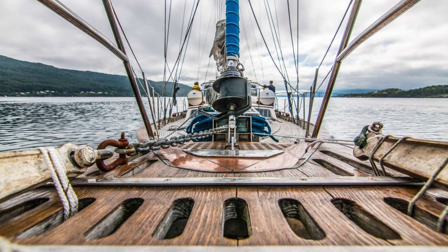 Das Bugdeck der Ylva (Eira Expeditions) zeigt gespannte Segel, maritime Ausrüstung und den Blick über einen norwegischen Fjord.