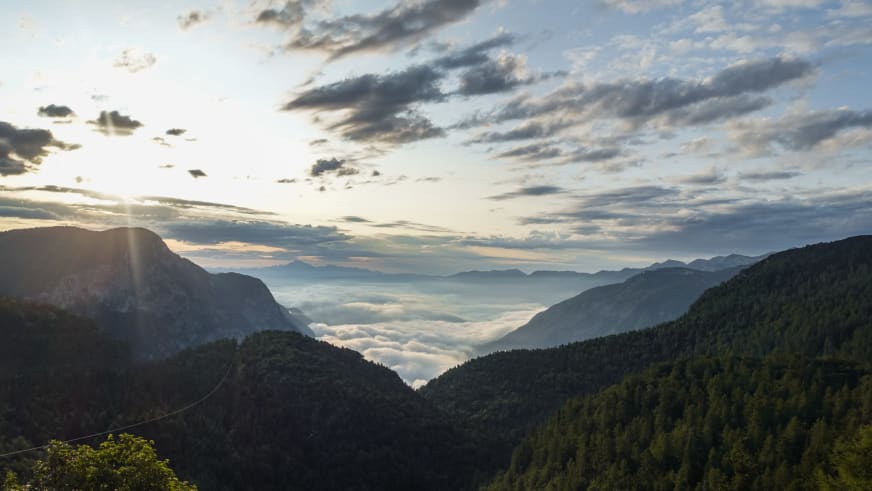Blick vom Dom na Komni durch ein V-förmiges Tal über eine geschlossene Wolkendecke in den Julischen Alpen.
