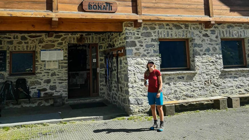 Außenansicht des Rifugio Alpino Walter Bonatti mit traditioneller Steinarchitektur und Wanderer vor dem Eingang.