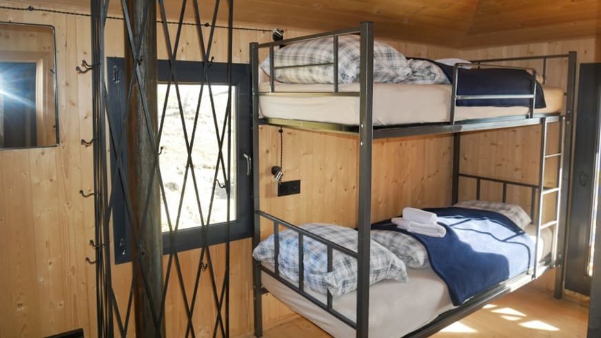Mehrbettzimmer der Berghütte Meria Keli mit Stockbetten und hellem Holzinterieur auf 2400 m Höhe.