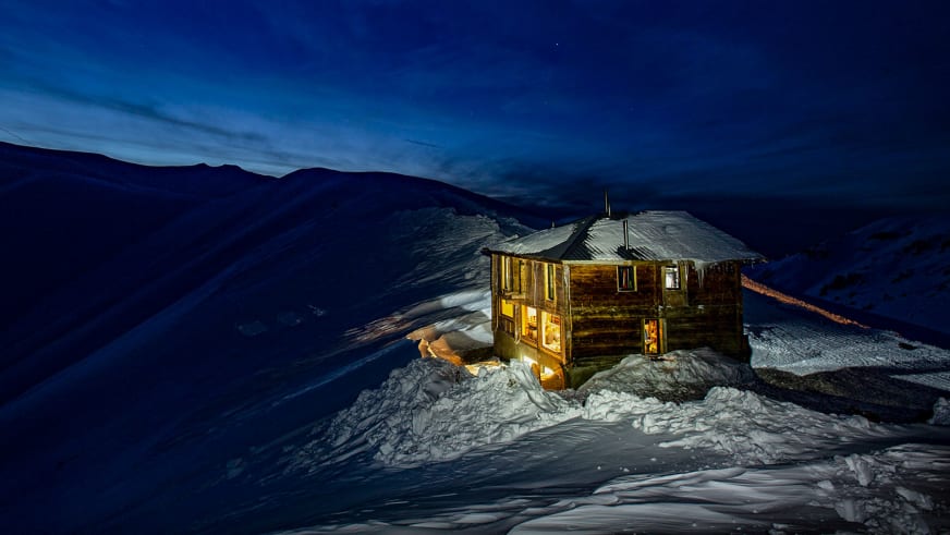 Die Berghütte Meria Keli steht nachts beleuchtet im Schnee auf 2400 m Höhe in der georgischen Berglandschaft.