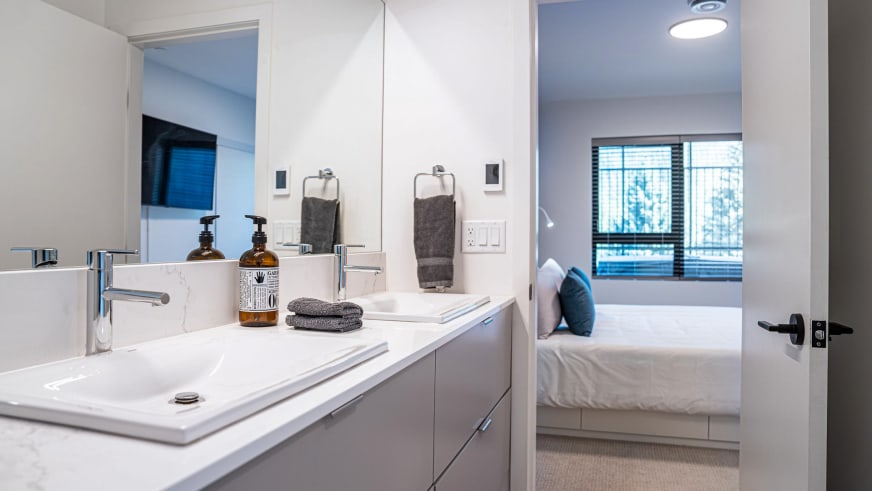 Offener Bad-Schlafbereich im Stoked Penthouse Revelstoke mit Doppelwaschtisch und angrenzendem Schlafzimmer.