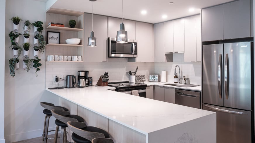 Moderne Küche im Stoked Penthouse Revelstoke mit weißer Kücheninsel und vier schwarzen Barhockern.