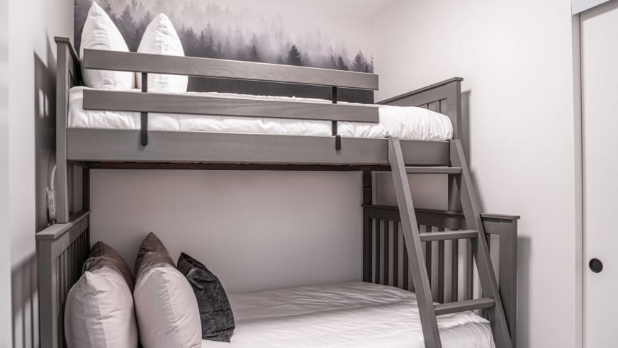 Mehrbettzimmer im Stoked Penthouse Revelstoke mit grauem Hochbett aus Holz und Fototapete mit Nadelbäumen.