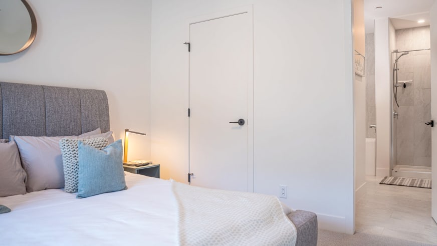 Schlafzimmer im Stoked Penthouse Revelstoke mit Doppelbett und angrenzendem Badezimmer mit Glasdusche.