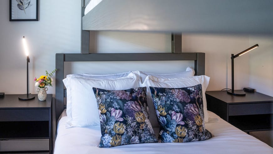 Schlafzimmer im Stoked Penthouse Revelstoke mit Metallrahmen-Bett und floralen Dekokissen in violett und blau.