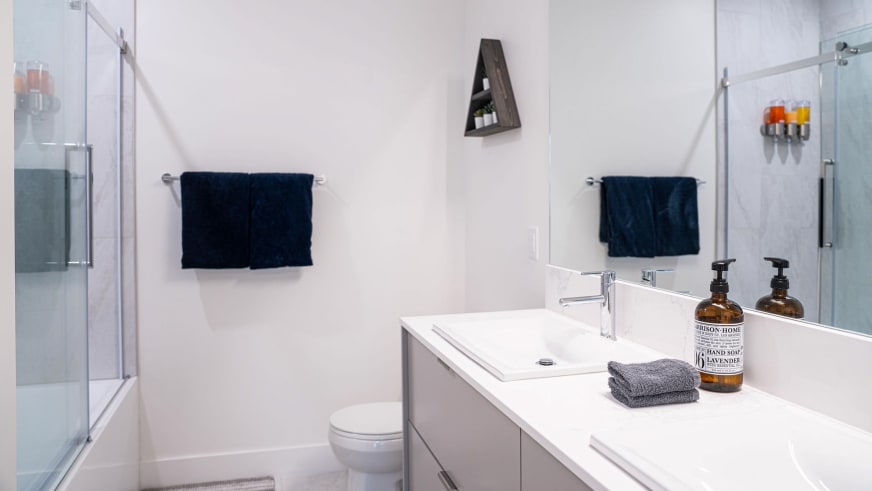 Badezimmer im Stoked Penthouse Revelstoke mit weißem Waschtisch, Glasdusche und LED-Beleuchtung.