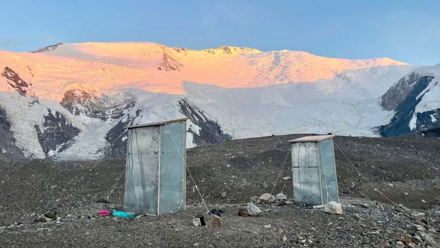 Blaue Toilettenhäuschen im Advanced Base Camp ABC Pik Lenin vor vergletscherter Bergkette im Abendlicht.
