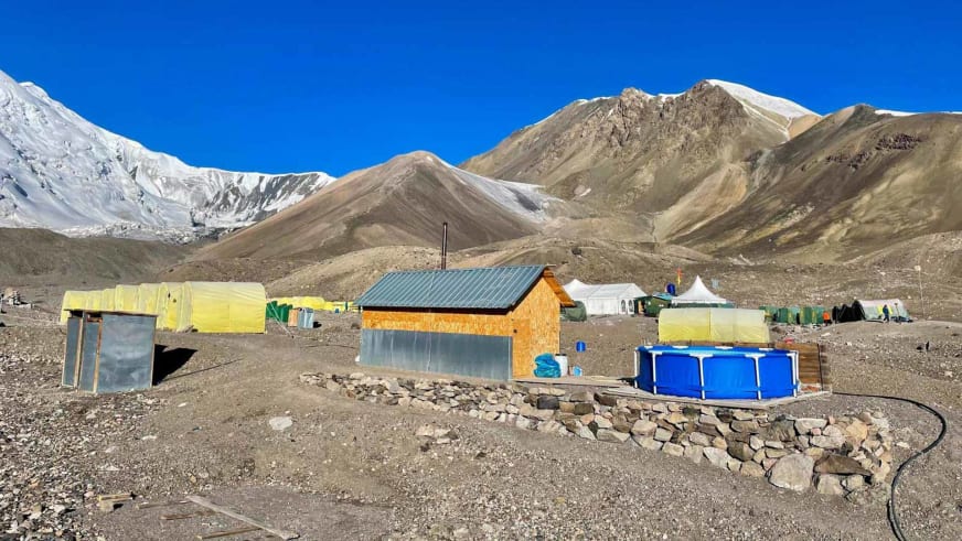 Küchengebäude und Wasserbecken im Advanced Base Camp ABC Pik Lenin zwischen gelben Expeditionszelten auf Steinplateau.