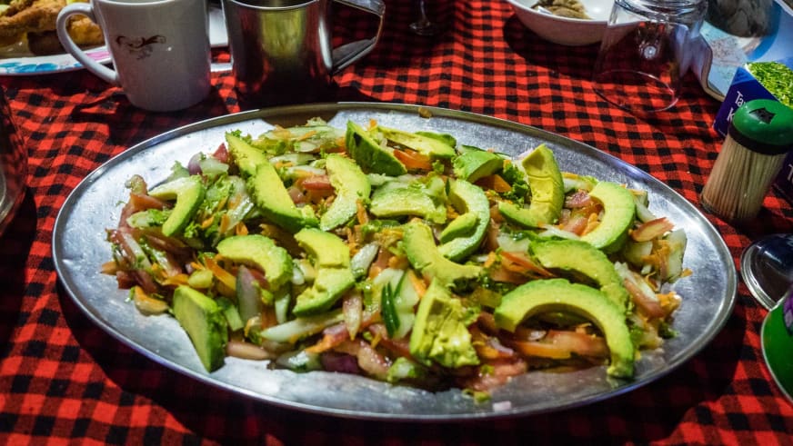 Frischer Avocado-Salat mit Gemüse auf Metallplatte in der Expeditionsküche des Zeltcamp am Kilimanjaro.