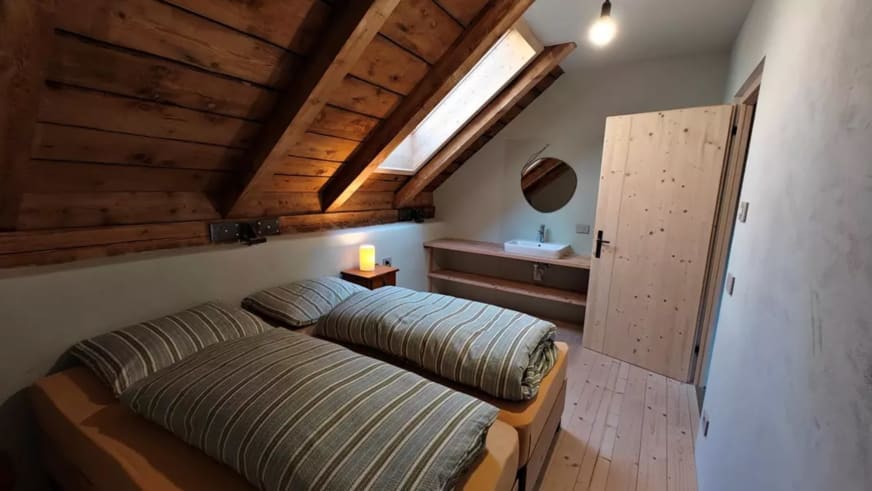 Dachgeschoss-Schlafzimmer der ANAS126 Lodge mit sichtbaren Holzbalken, zwei Einzelbetten und Zirbenholz-Kleiderschrank.