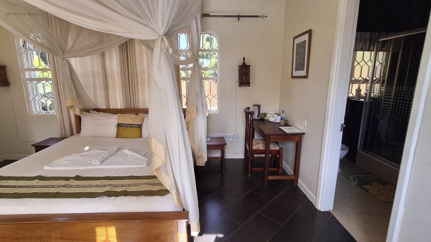 Doppelzimmer im Entebbe Palm Hotel mit Himmelbett, weißem Moskitonetz und tropischem Ausblick durch Sprossenfenster.