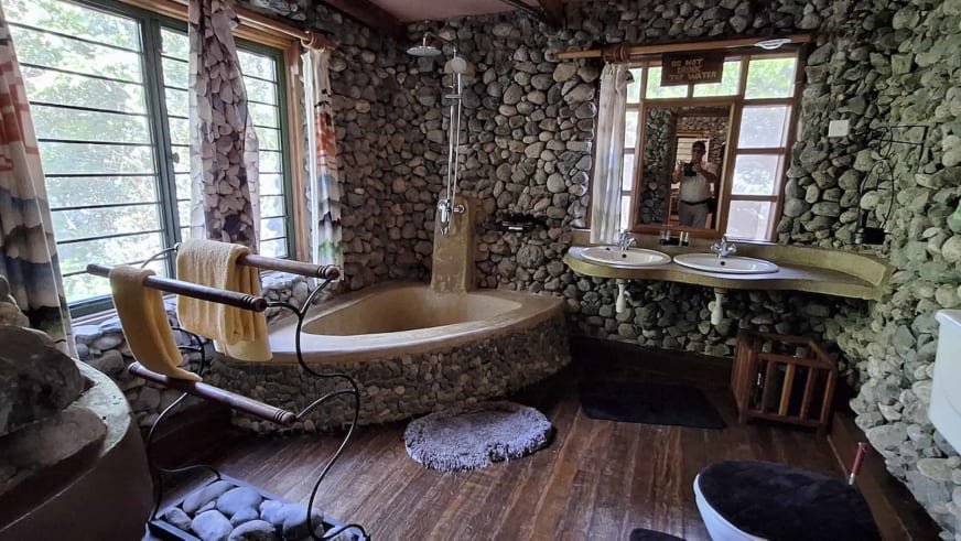Badezimmer in der Snow Heights Lodge mit vollständiger Flussstein-Verkleidung, freistehender Badewanne und Regendusche.