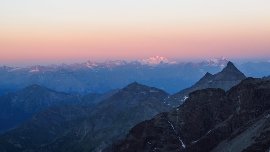 Hochtour in den Walliser Alpen: Panoramablick auf den Mont Blanc und umliegende Gipfel im rosa Dämmerungslicht.