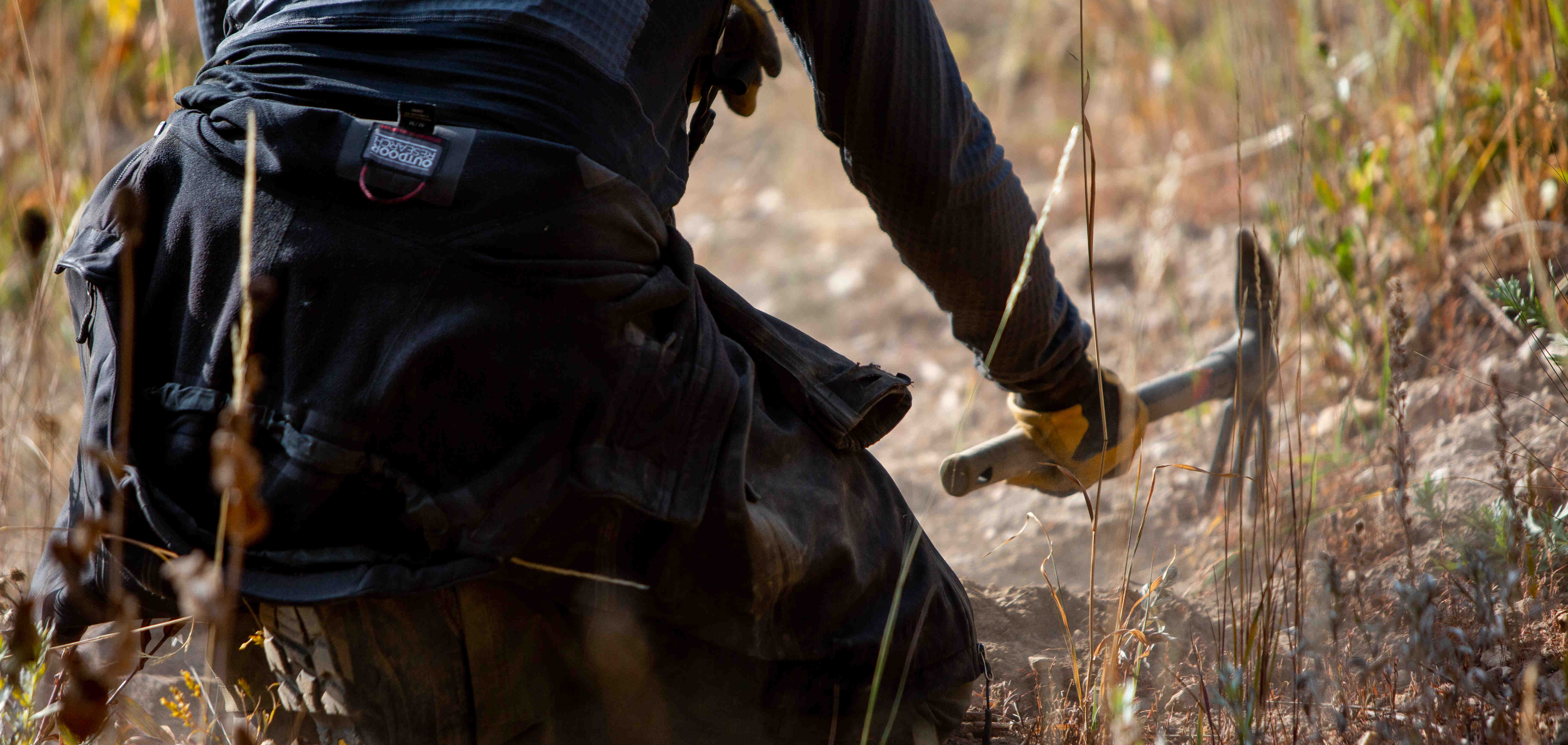 Alta employee swinging a hand pick to dig a hole for tree planting