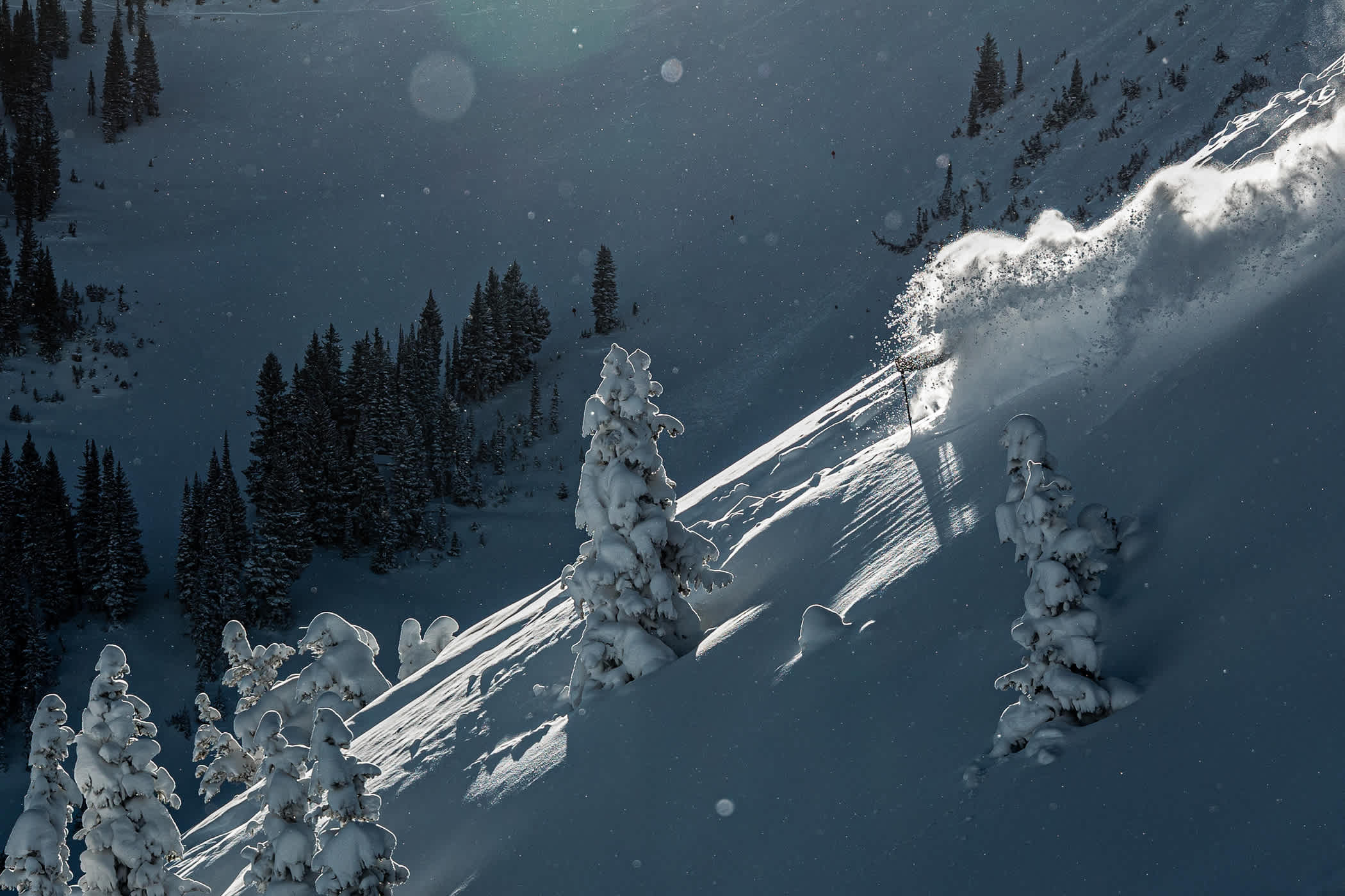 A skier decends a powder-filled mountain in moody light